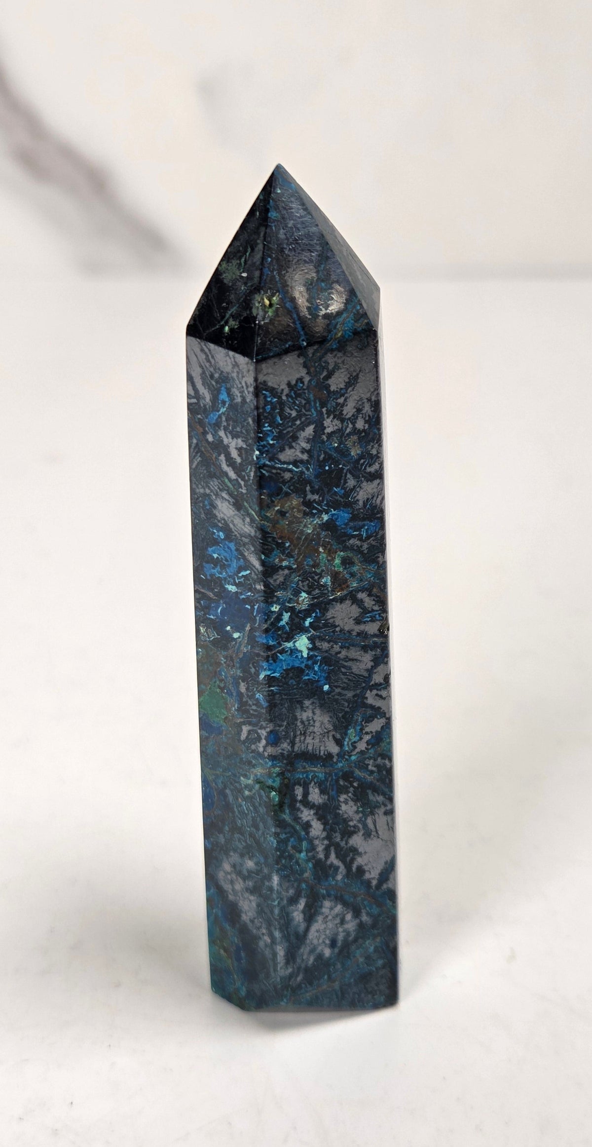 Blue-green Azurite & Chrysocolla crystal point on a white surface with a gray background