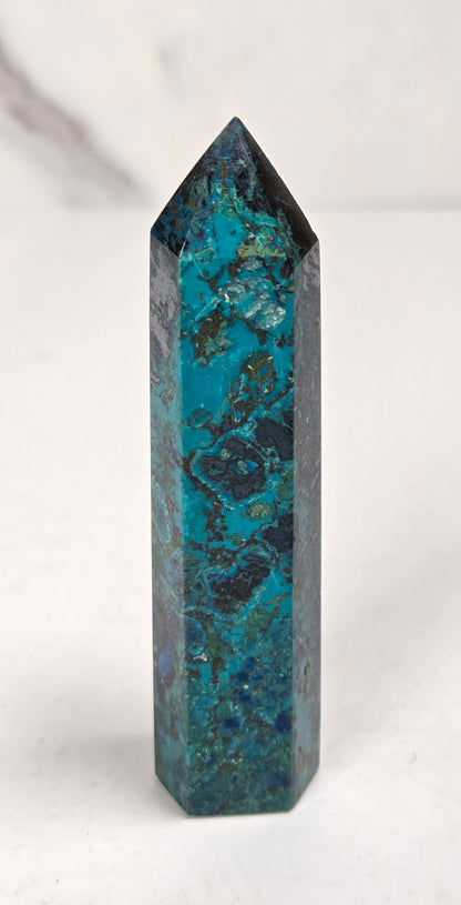 Blue-green Azurite & Chrysocolla crystal point on a white surface with a gray background