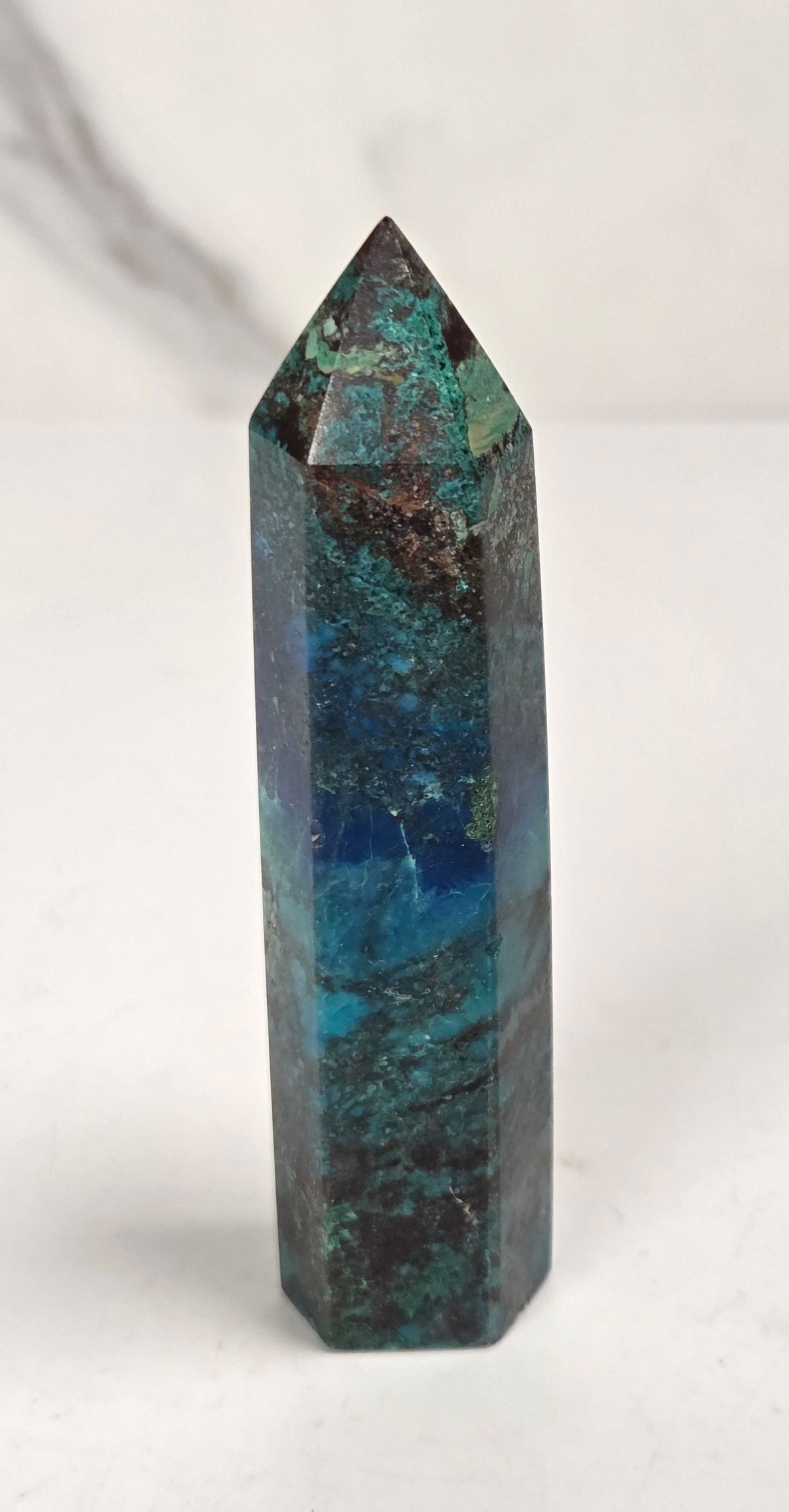 Blue-green Azurite & Chrysocolla crystal point on a white surface with a gray background