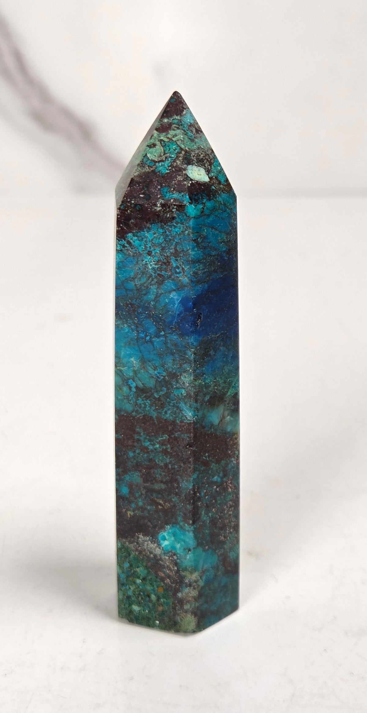 Blue-green Azurite & Chrysocolla crystal point on a white surface with a gray background