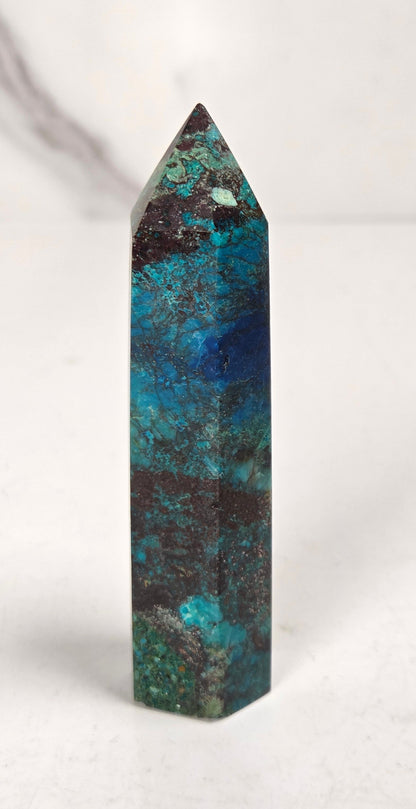 Blue-green Azurite & Chrysocolla crystal point on a white surface with a gray background