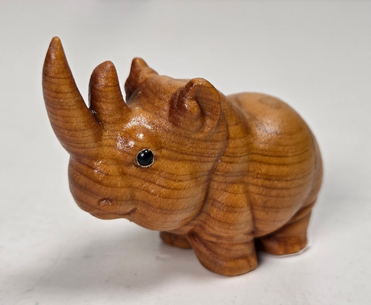 A small wooden rhinoceros figurine, crafted from light brown wood with visible grain, set against a neutral light gray background.
