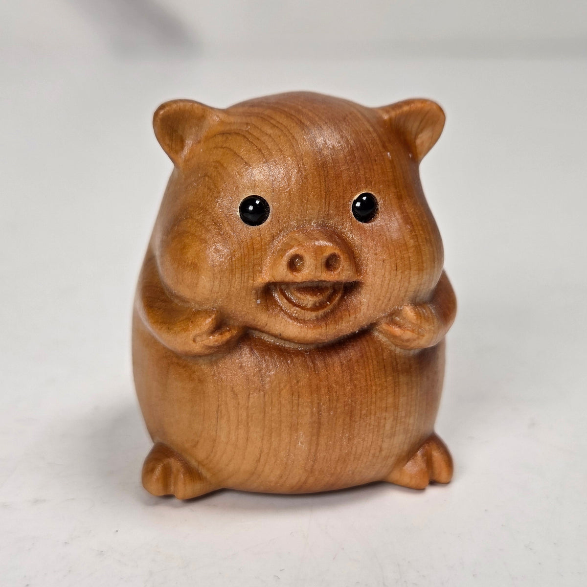 A small wooden pig figurine, crafted from light brown wood with visible grain, set against a neutral light gray background.
