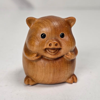 A small wooden pig figurine, crafted from light brown wood with visible grain, set against a neutral light gray background.