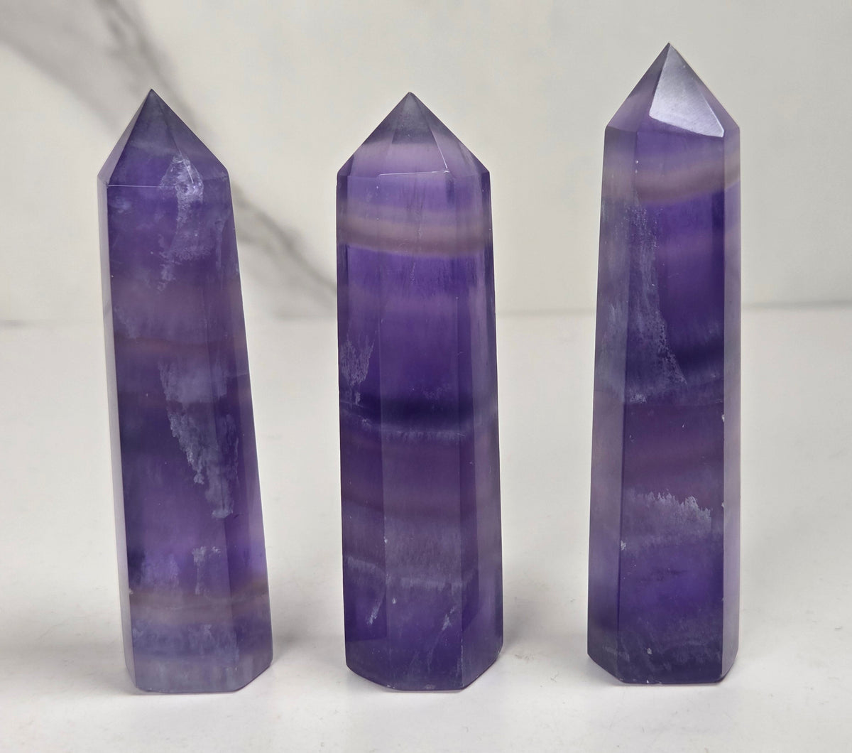 Set of 3 purple fluorite points with different color bands against a marbled background