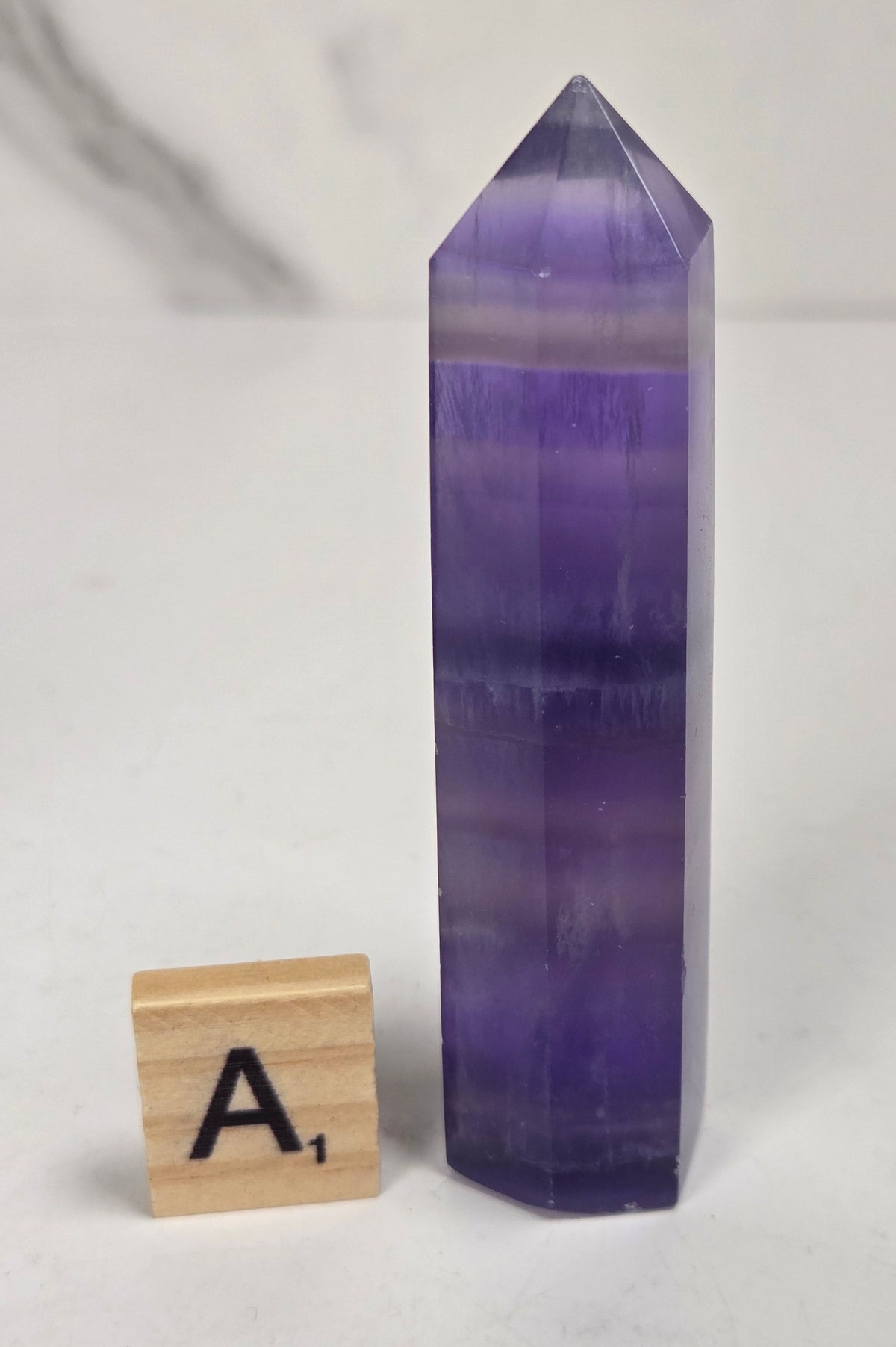 Purple fluorite tower with bands of color and a scrabble tile on a marbled background