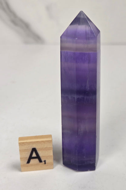 Purple fluorite tower with bands of color and a scrabble tile on a marbled background