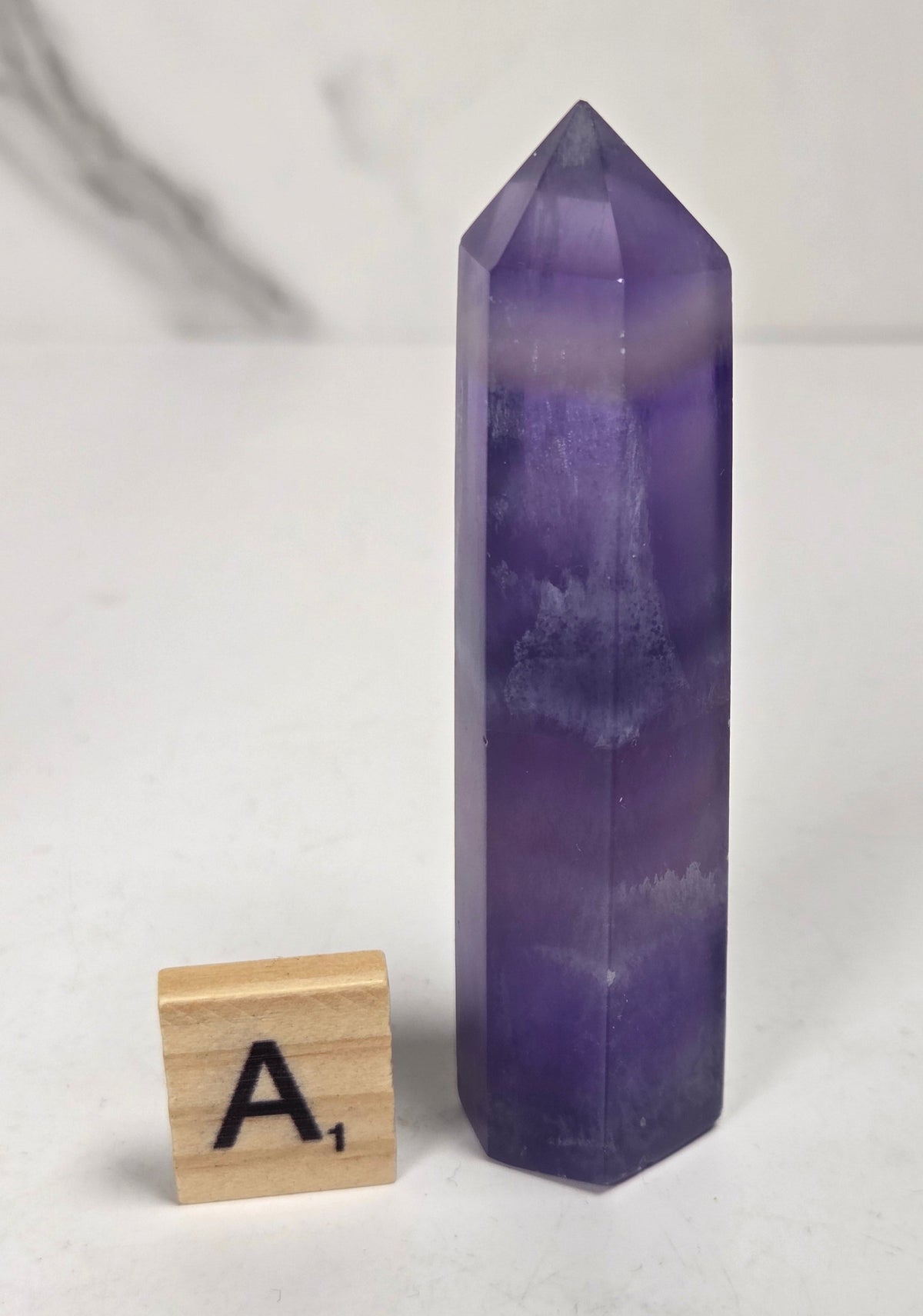 Purple fluorite tower with bands of color and a scrabble tile on a marbled background