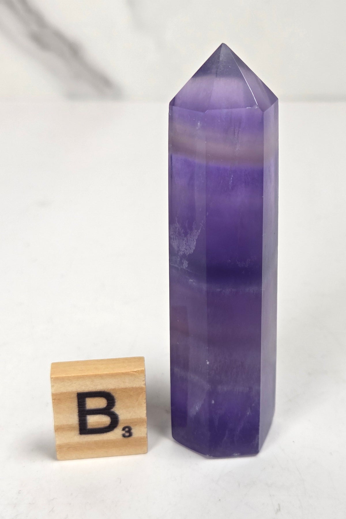 Purple fluorite tower with bands of color and a scrabble tile on a marbled background