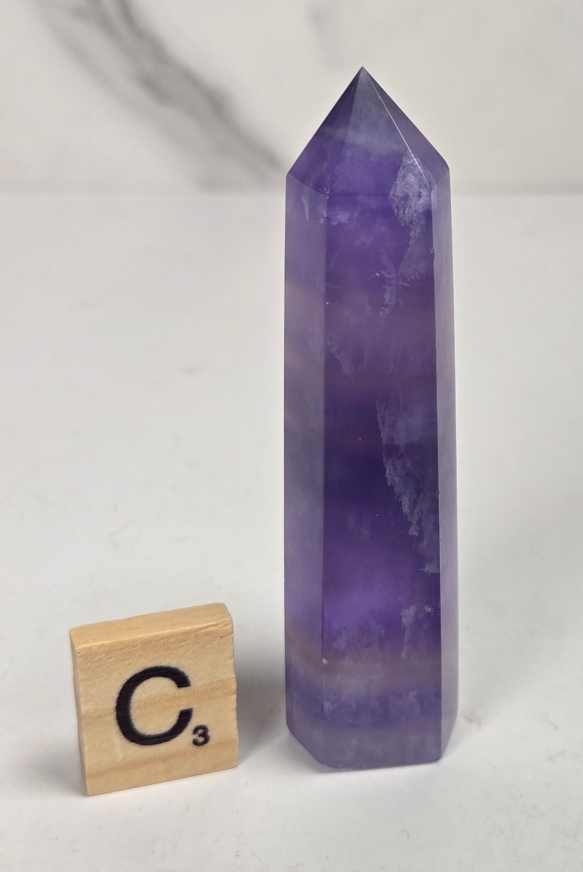 Purple fluorite tower with bands of color and a scrabble tile on a marbled background