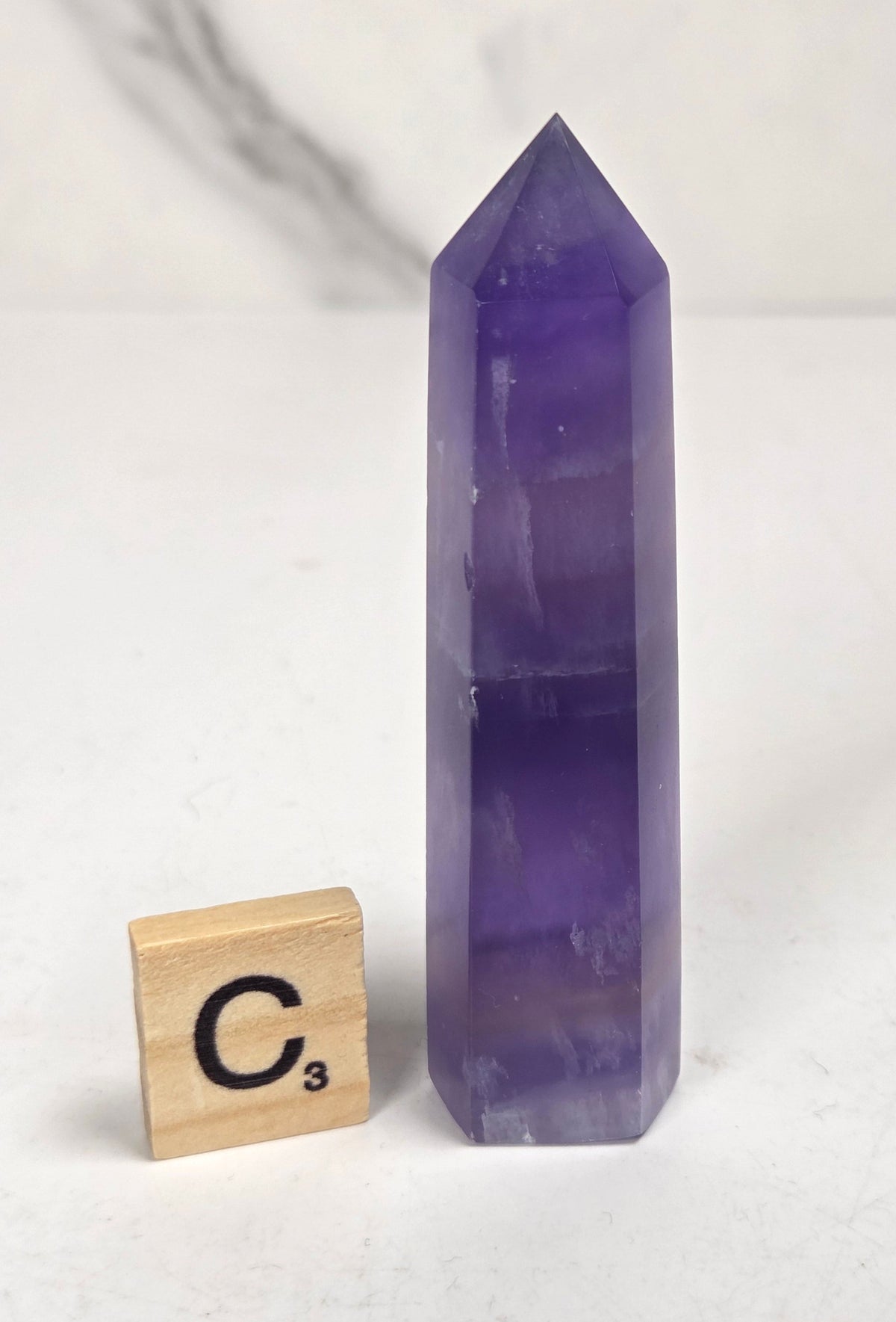 Purple fluorite tower with bands of color and a scrabble tile on a marbled background