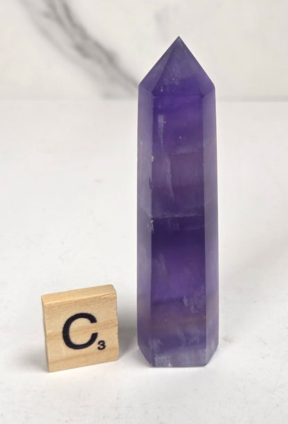Purple fluorite tower with bands of color and a scrabble tile on a marbled background