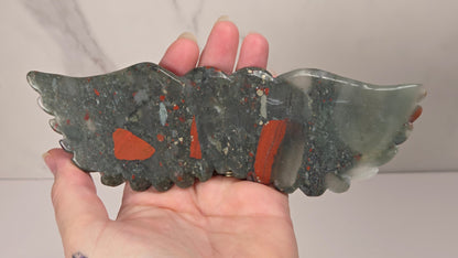 Hand holding a crystal heart with wings carving with black, grey, red and gold coloring against a white background