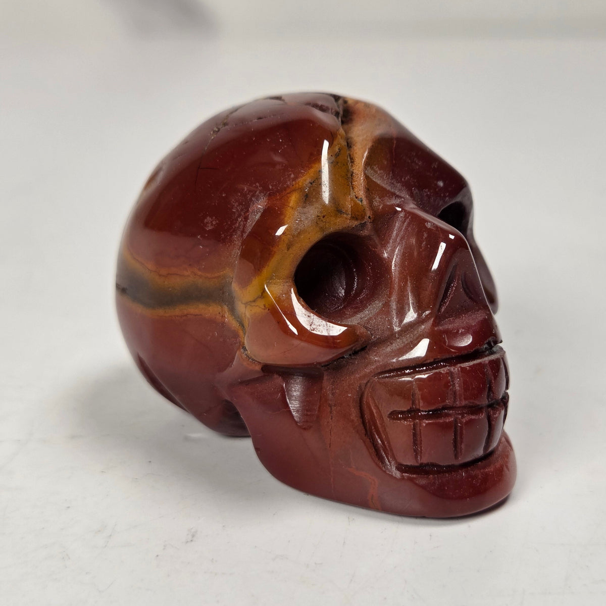 Red and yellow mookaite crystal skull carving on a white background