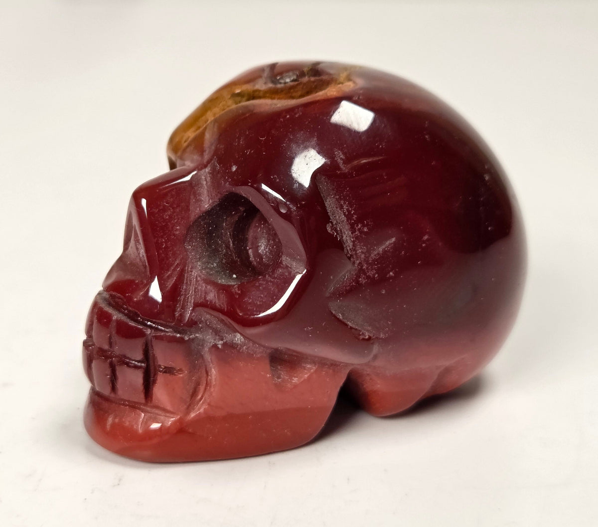 Red and yellow mookaite crystal skull carving on a white background