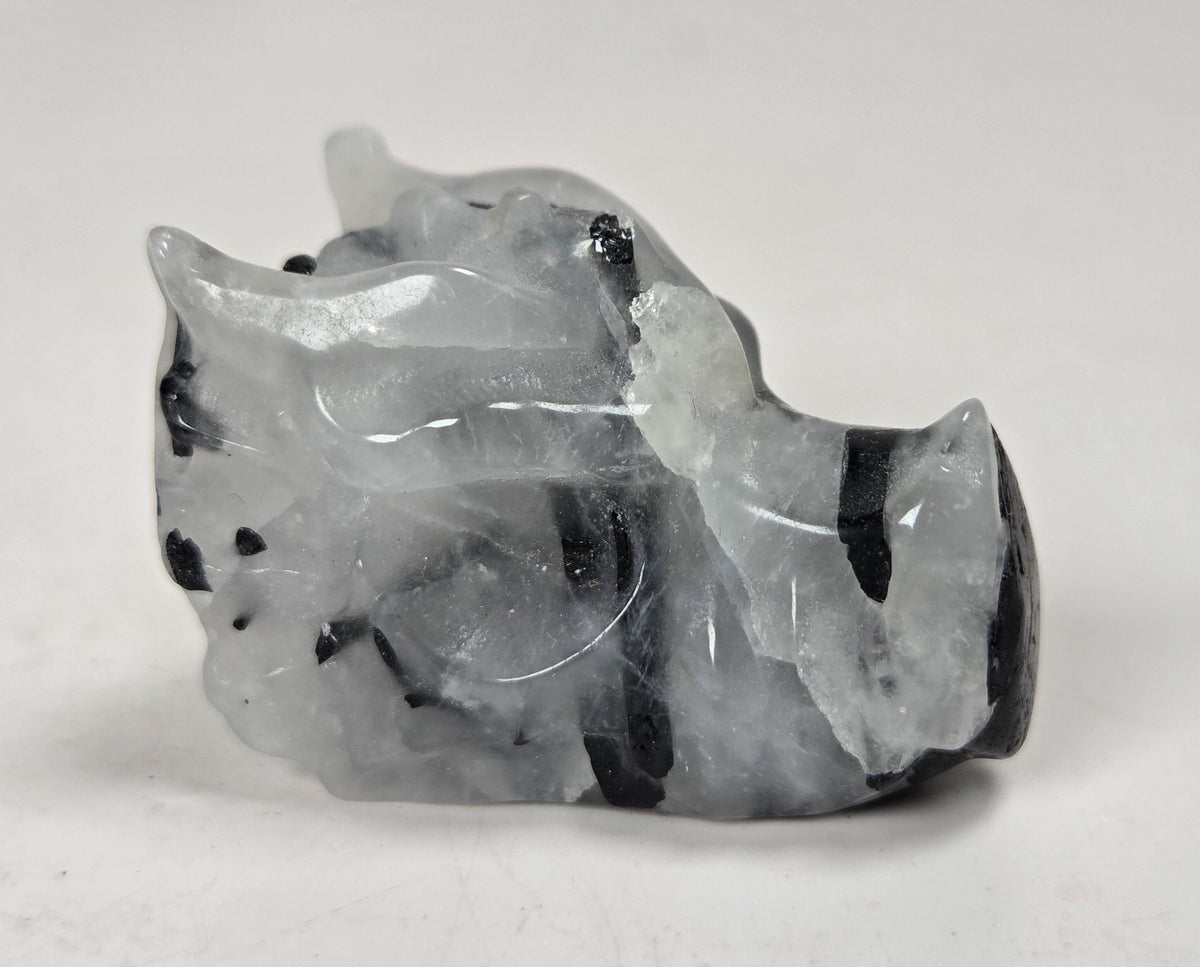 A small dragon head sculptures made of Quartz with black tourmaline inclusions on a white background