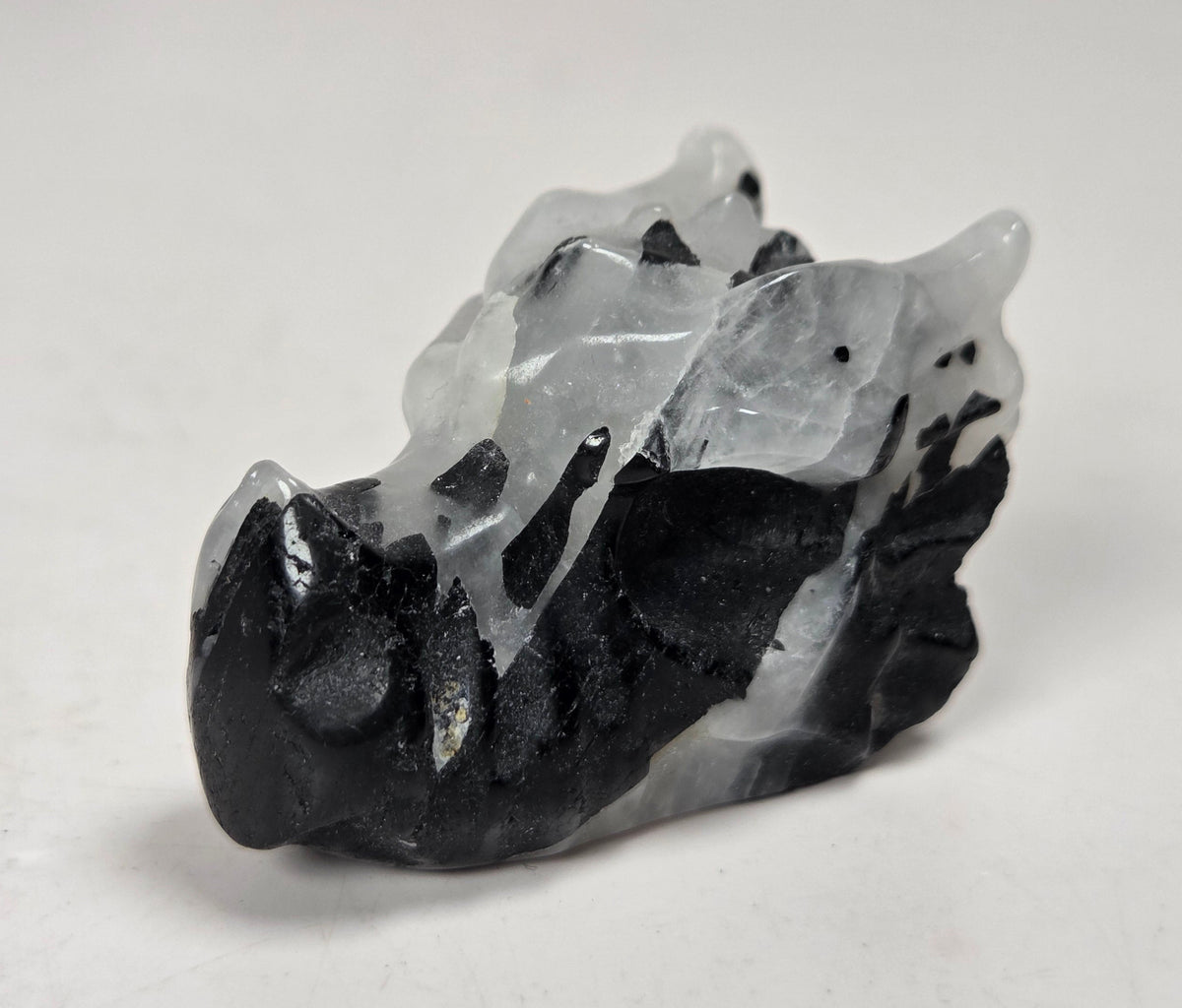 A small dragon head sculptures made of Quartz with black tourmaline inclusions on a white background
