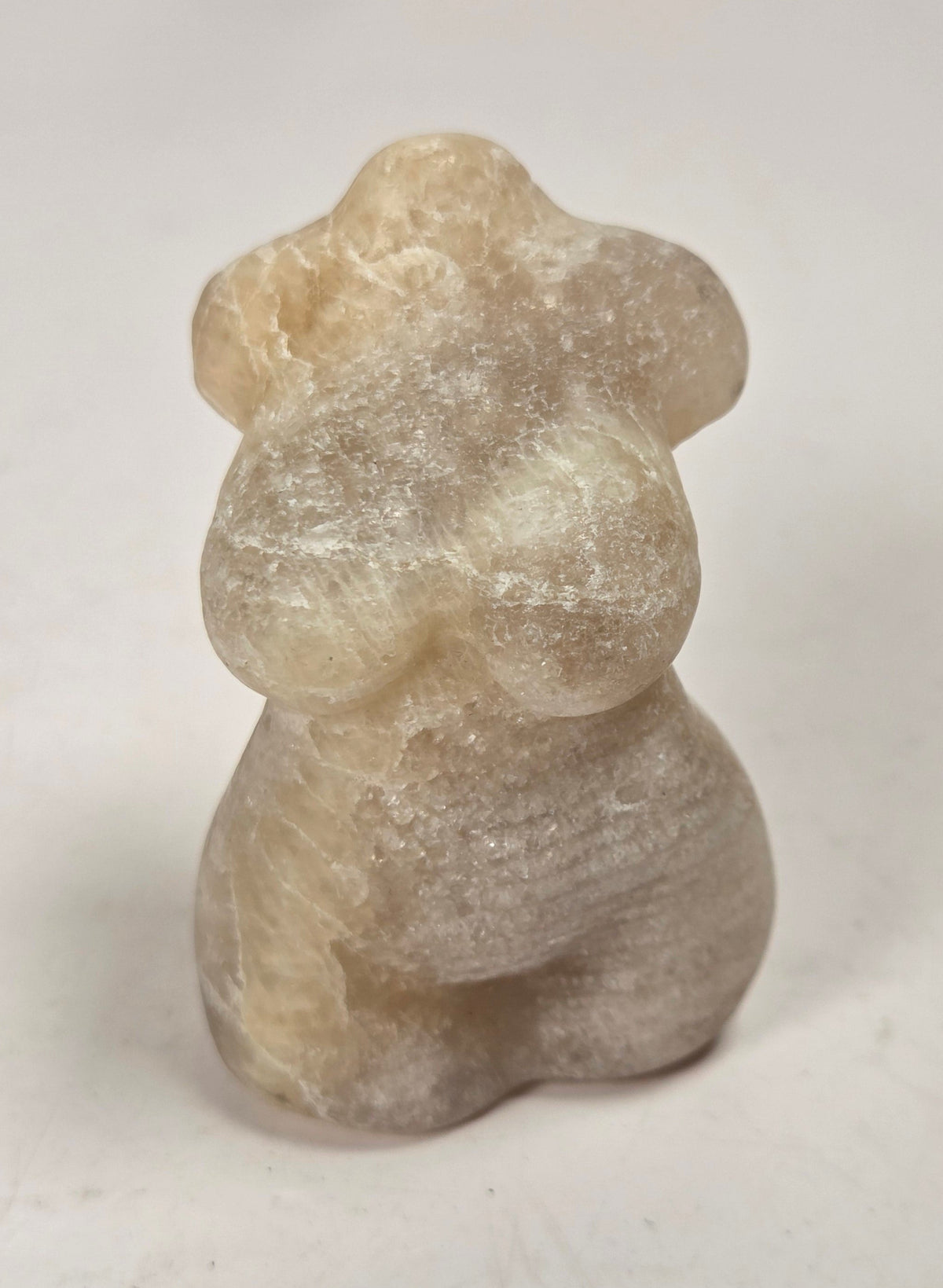 A  small carved stone figurine with a pearlescent, milky appearance and subtle blue iridescence, set against a light marble-patterned background.