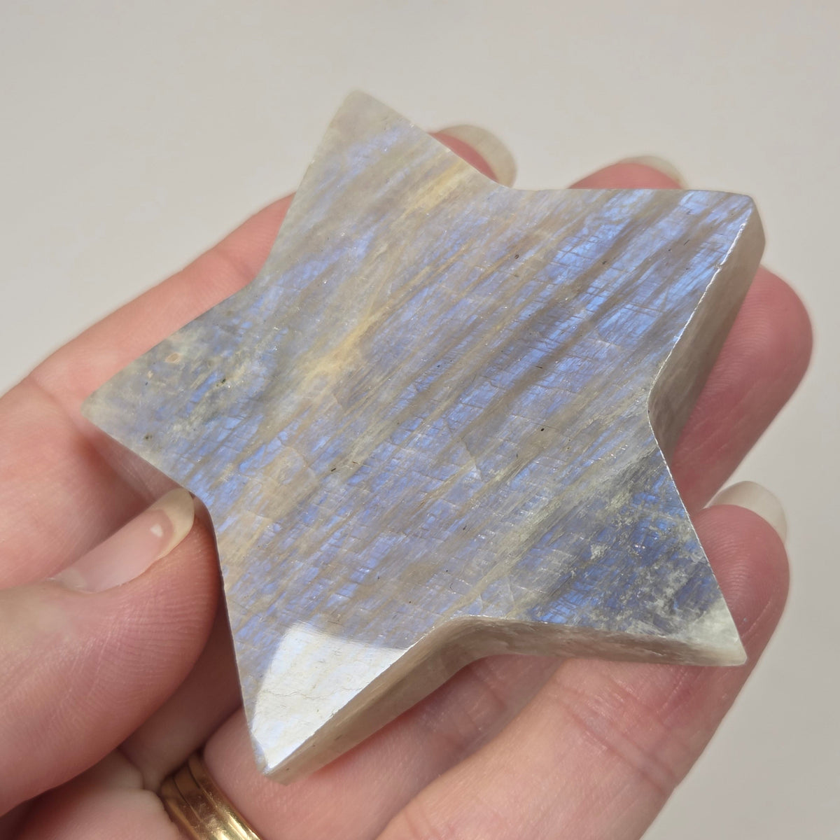crystal star shaped carving made of moonstone showing blue flash being held in a hand against a white background