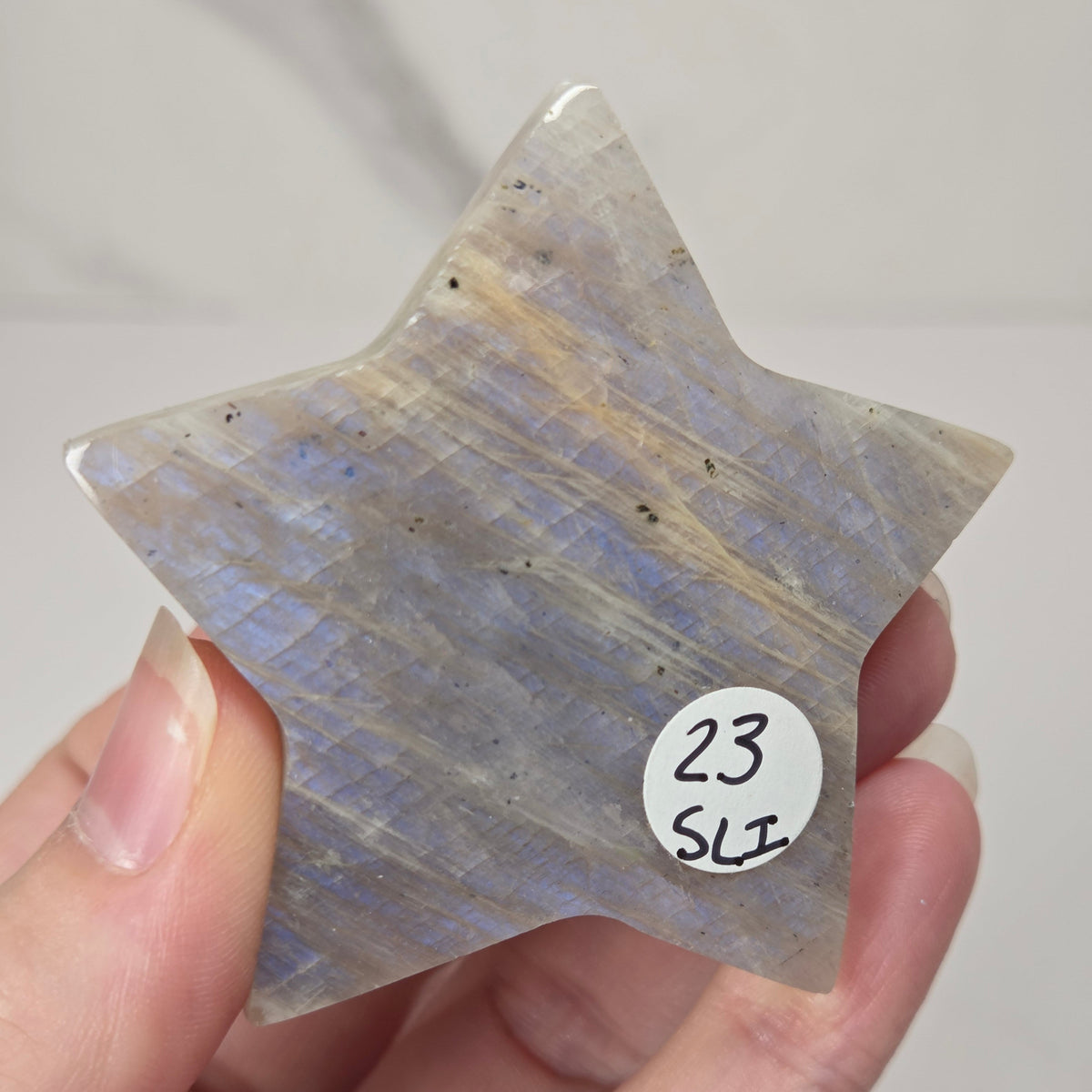 crystal star shaped carving made of moonstone showing blue flash being held in a hand against a white background