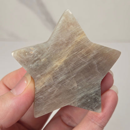 crystal star shaped carving made of moonstone showing blue flash being held in a hand against a white background