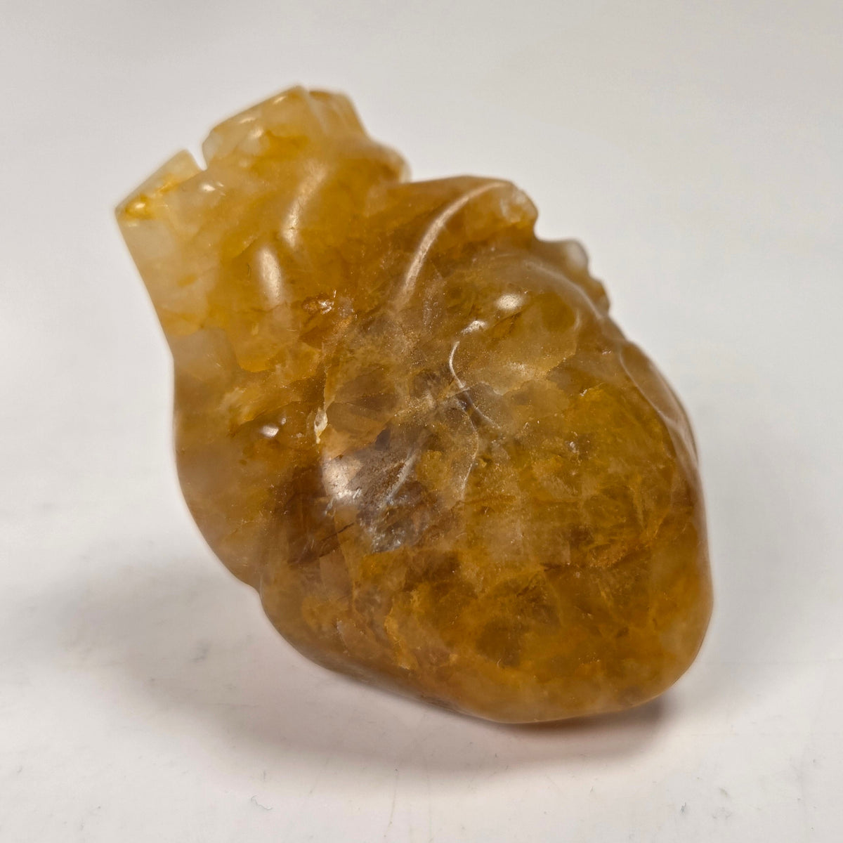 A small carved translucent heart-shaped stone pendant with gold coloring, photographed against a softly blurred light background.