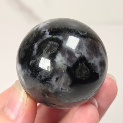 Person holding a dark marbled crystal sphere against a neutral background