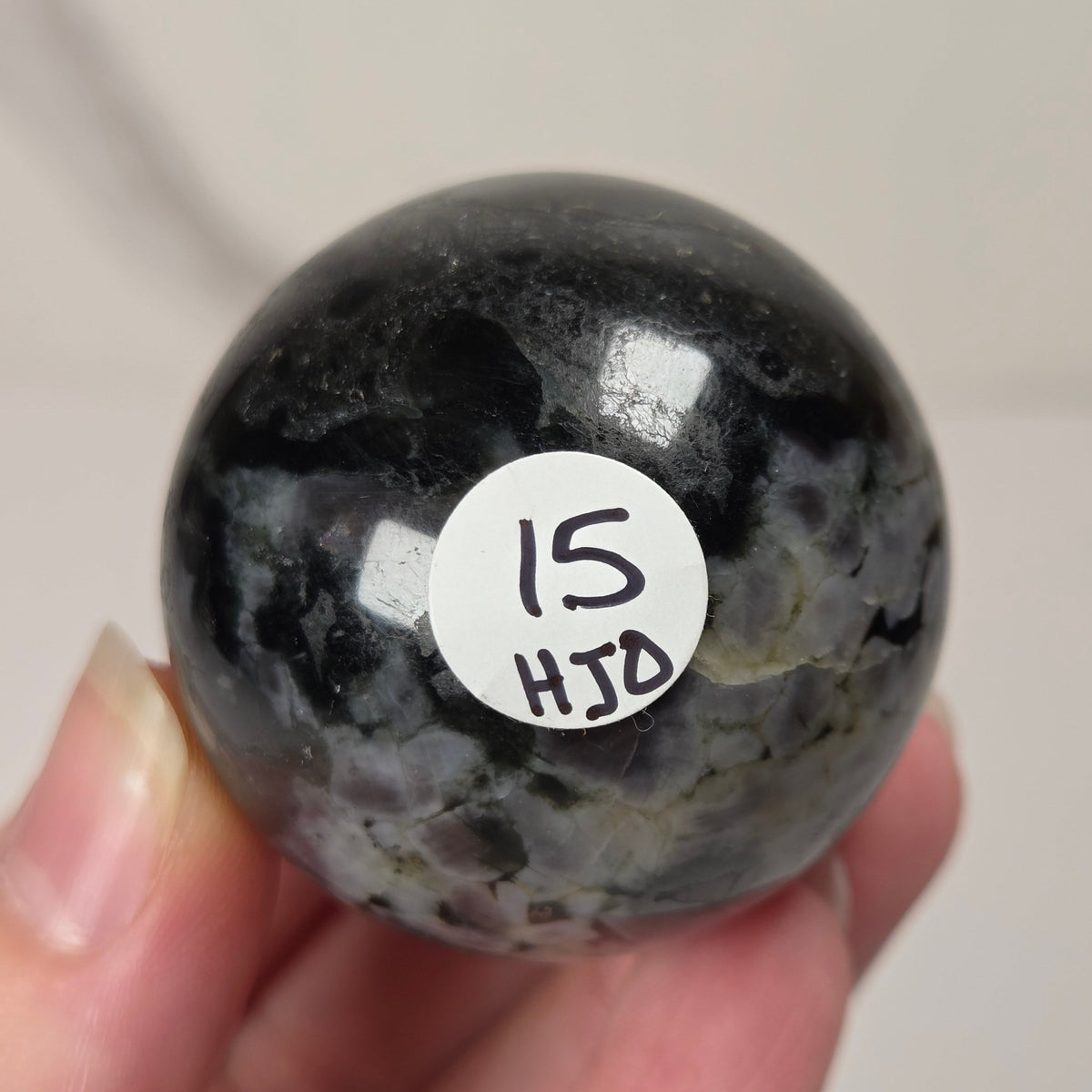 Person holding a dark marbled crystal sphere against a neutral background