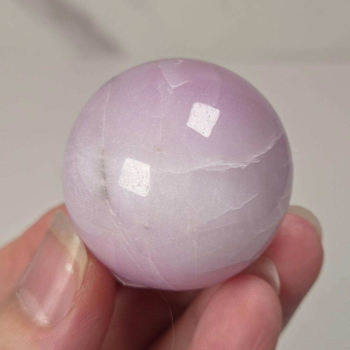 Hand holding a purple and white crystal sphere against a neutral background