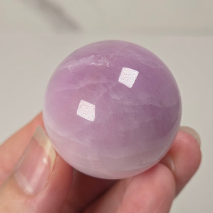 Hand holding a purple and white crystal sphere against a neutral background