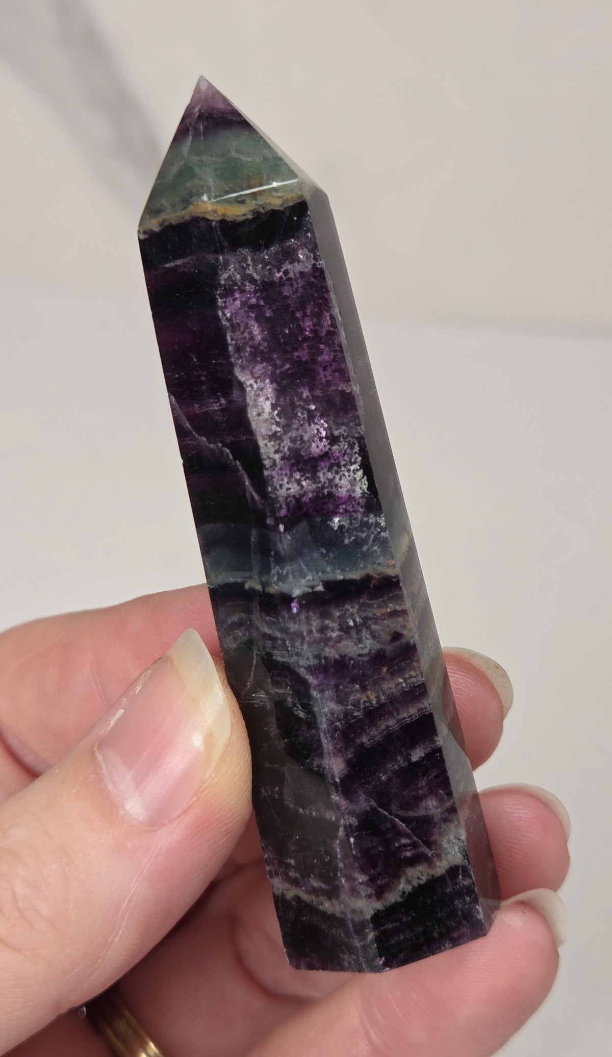 Hand holding a colorful banded fluorite tower with green and purple coloring against a white background
