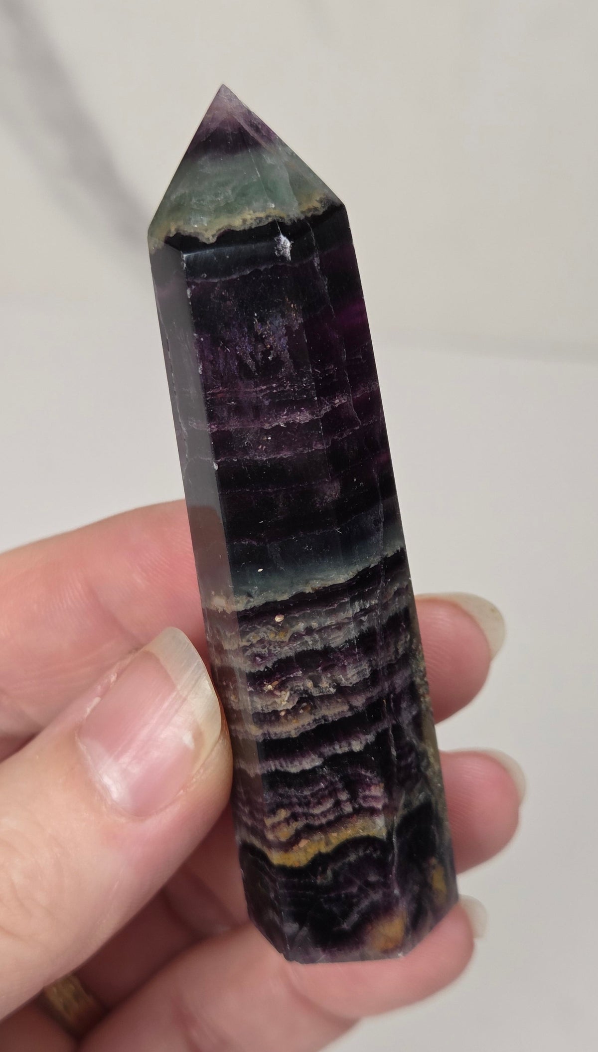 Hand holding a colorful banded fluorite tower with green and purple coloring against a white background