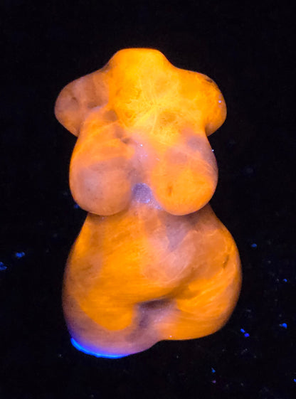 Sculpture of a goddess body made of Sodalite under UV light showcasing a bright orange color displayed on a black background