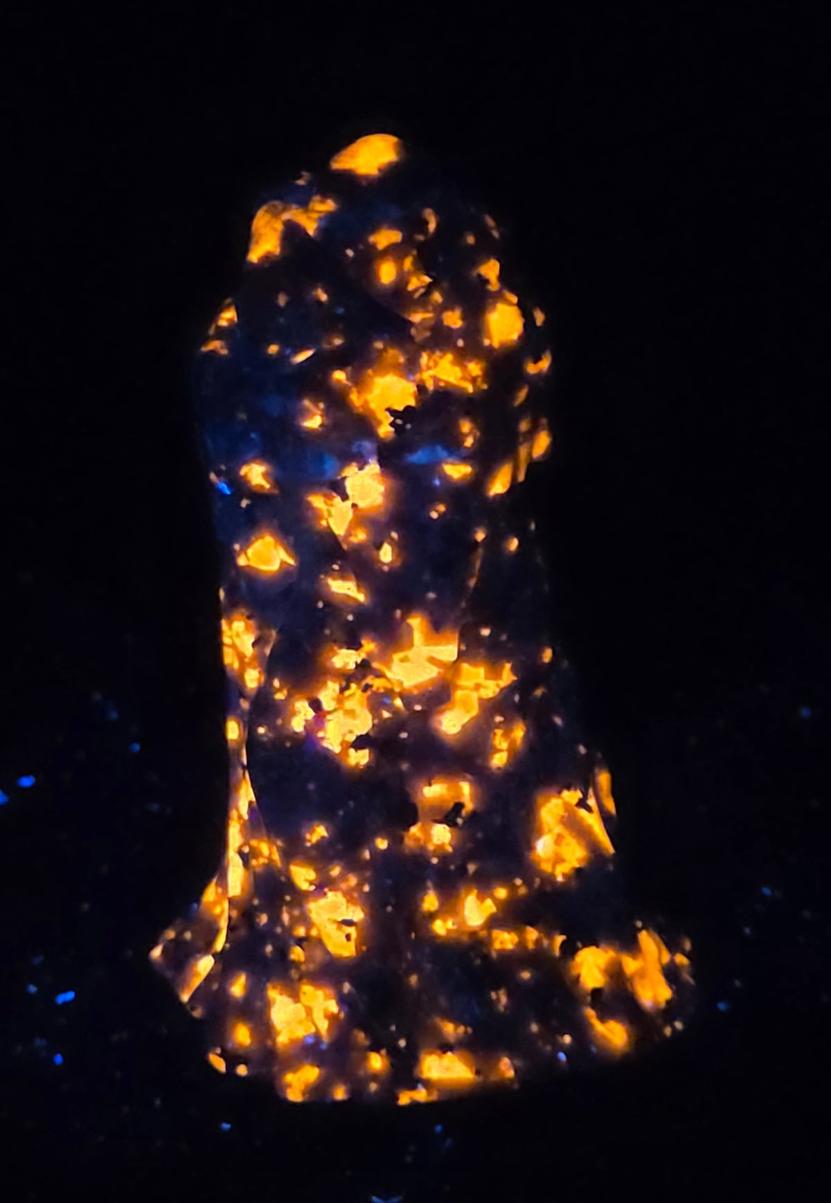 A black textured sculpture of a hooded figure, resembling a grim reaper or raven, under UV light showcasing a bright orange glow.