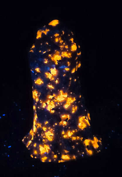 A black textured sculpture of a hooded figure, resembling a grim reaper or raven, under UV light showcasing a bright orange glow.