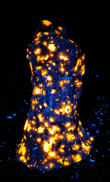 A black textured sculpture of a hooded figure, resembling a grim reaper or raven, under UV light showcasing a bright orange glow.