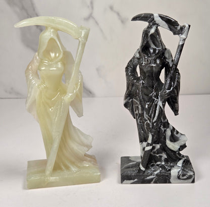 faceless lady reaper carvings made of a golden tan color and a marbled black and white mineral against a marbled white background
