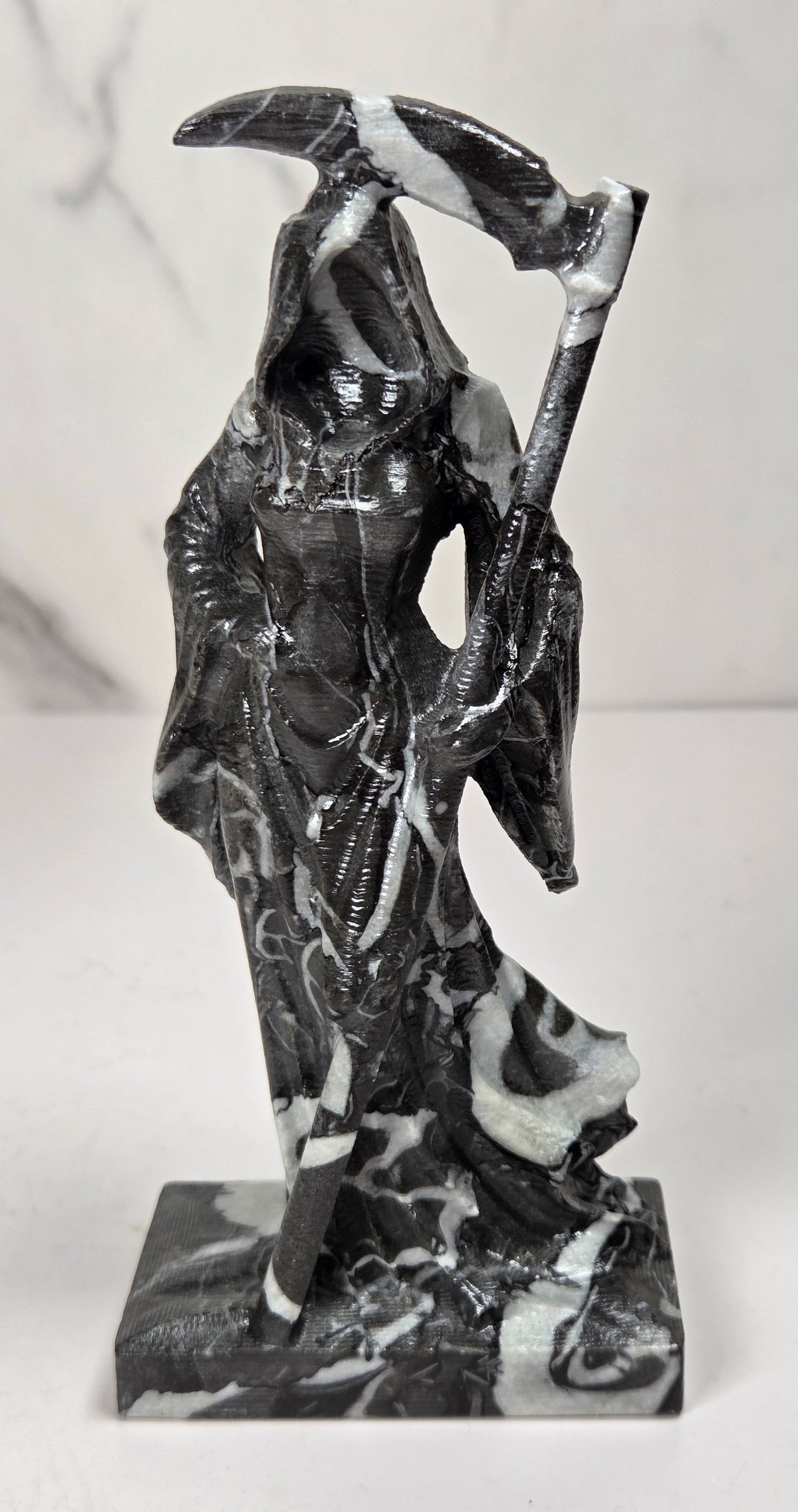 faceless lady reaper carving made of a  marbled black and white mineral against a marbled white background