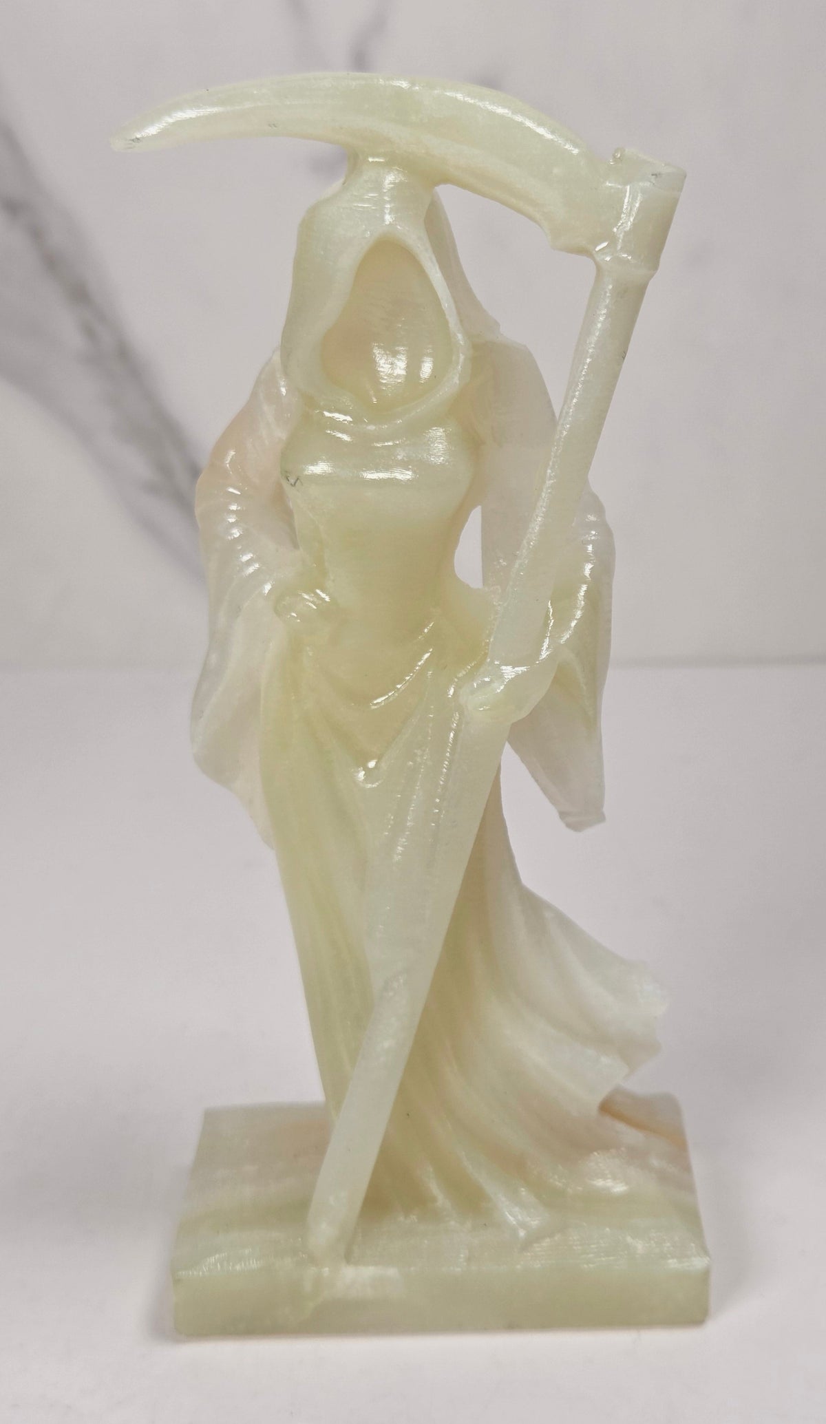 faceless lady reaper carving made of a  off-white mineral against a marbled white background