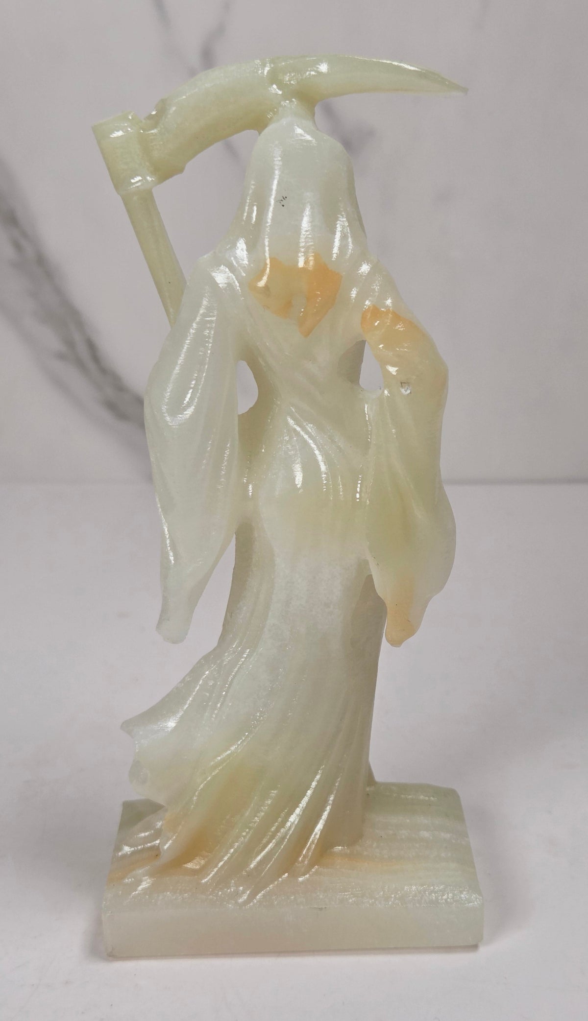 faceless lady reaper carving made of a  off-white mineral against a marbled white background