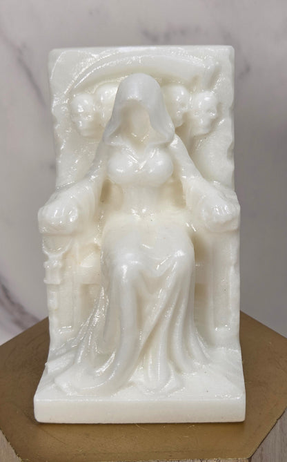 Carving of a faceless woman wearing a robe, sitting on a chair, in white jade, on a wooden stand against a marble background