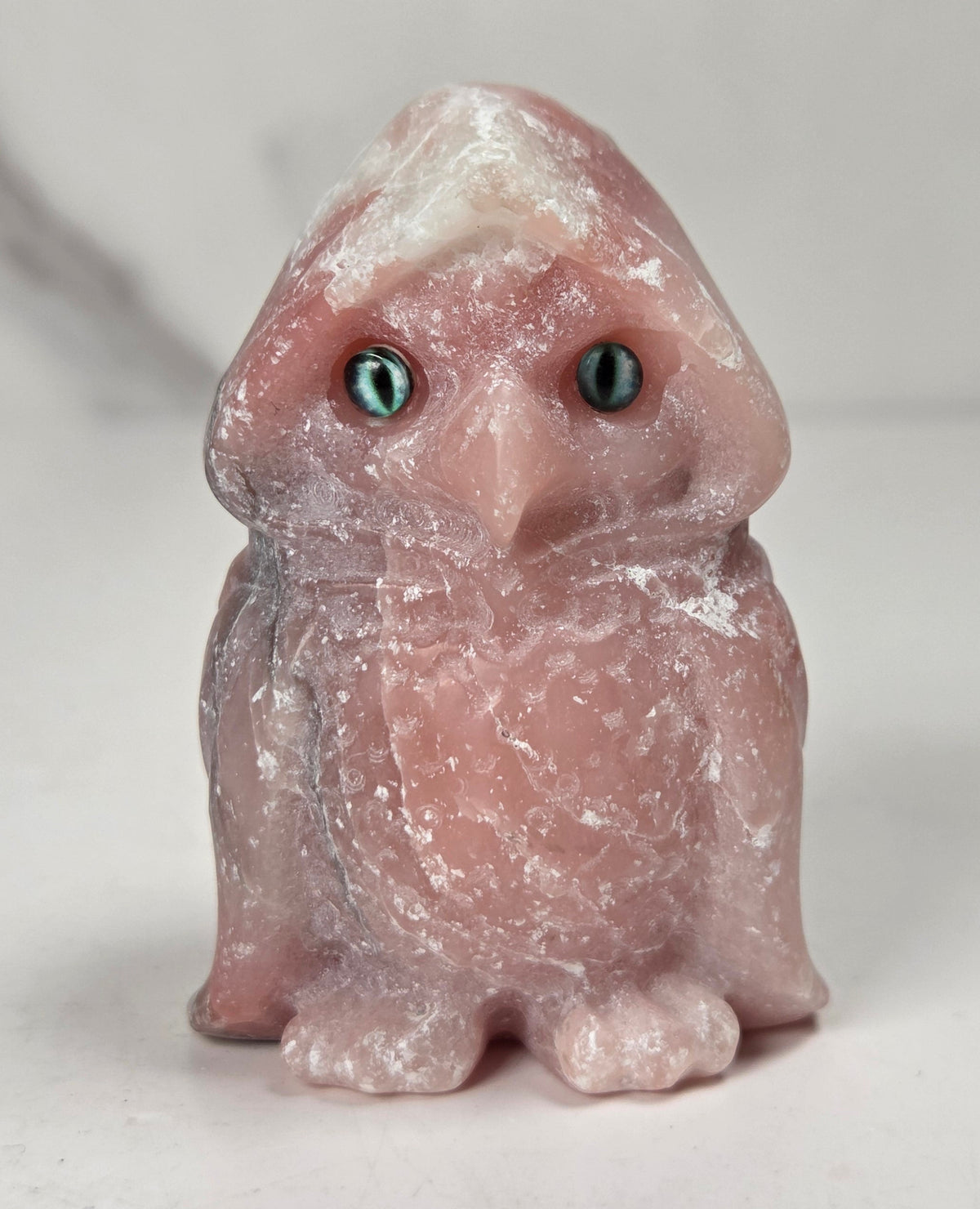 A small carved stone owl figurine with a hooded head and bright green eyes, standing on a plain light background.