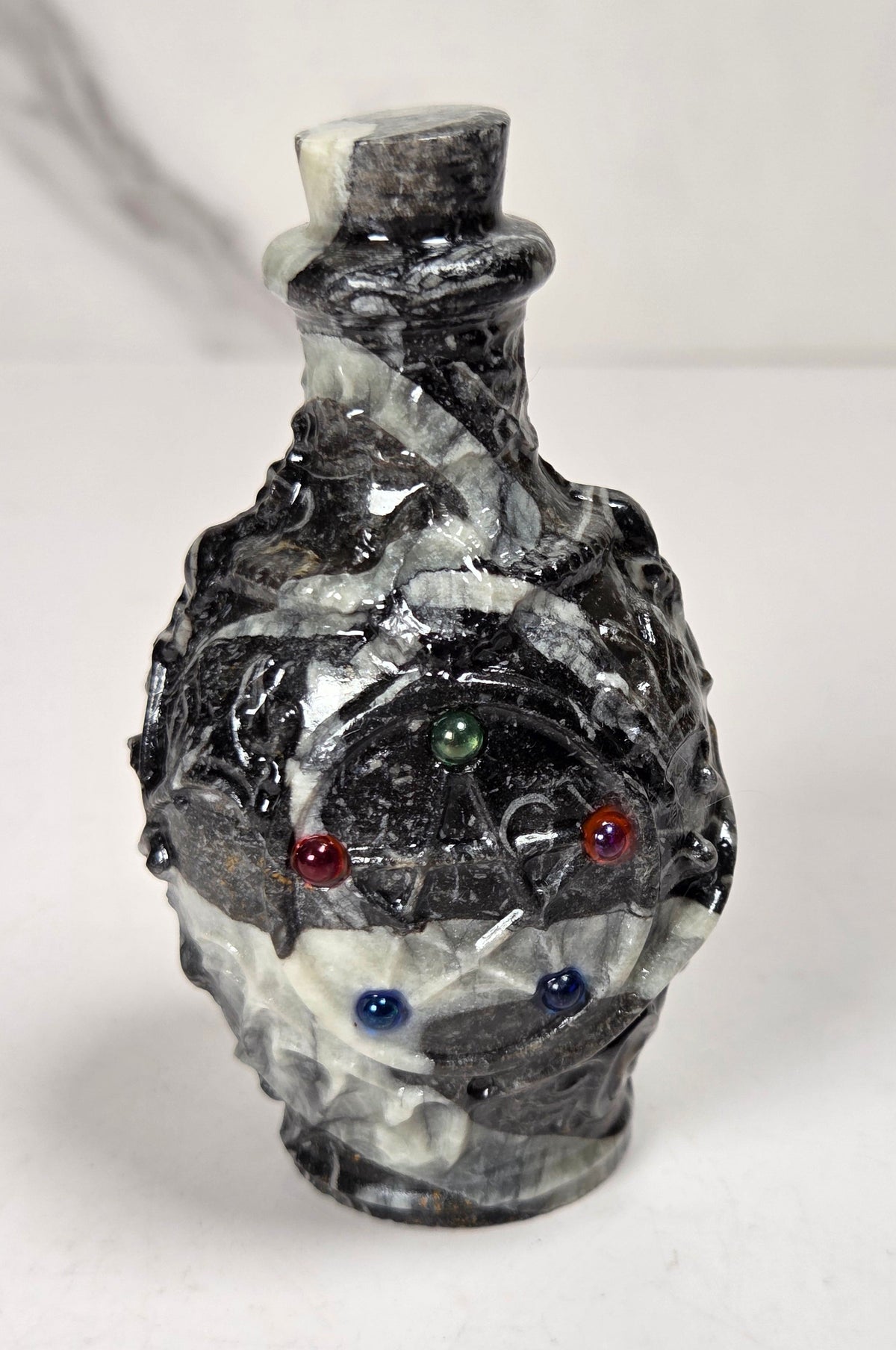 A small sculptural bottle or vase made of polished black and white marbled stone, with a star and small beads against a light marble-patterned background.