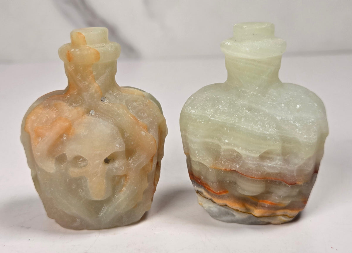 A pair of small crystal bottles shaped like skulls, with narrow necks and stoppers, photographed on a plain light background.