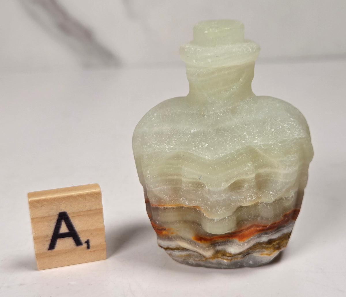 A small crystal bottle shaped like a skull, with a narrow neck and stopper, photographed on a plain light background with a scrabble wood tile.