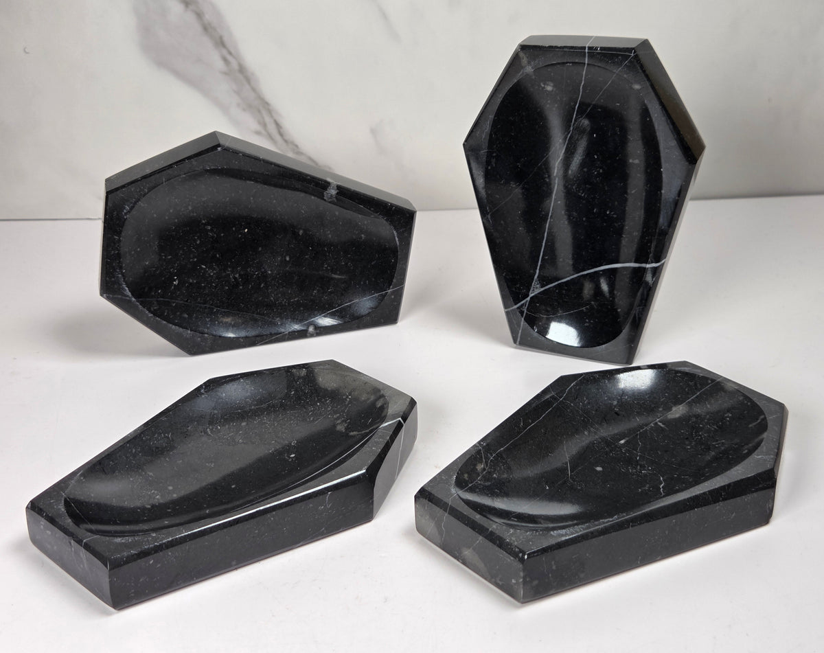 Black marble coffin shaped trinket bowls against a marbled background