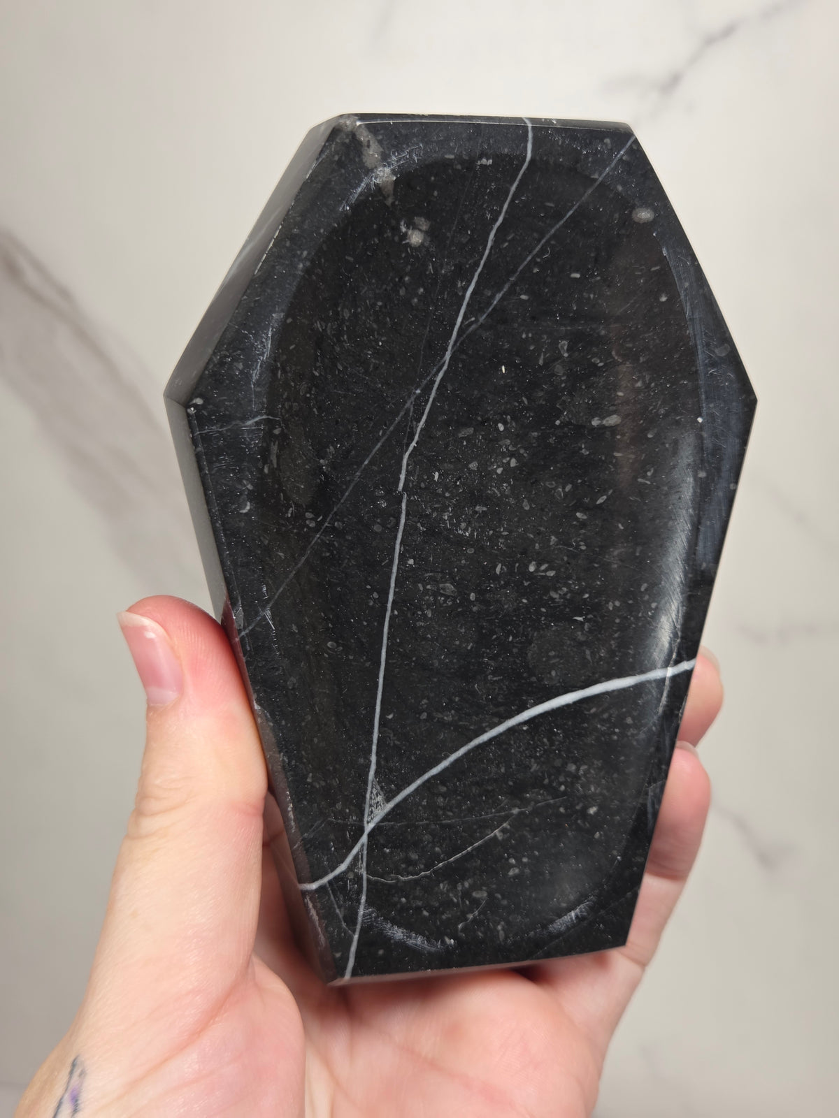 Hand holding a black marble coffin shaped trinket bowl against a marbled background