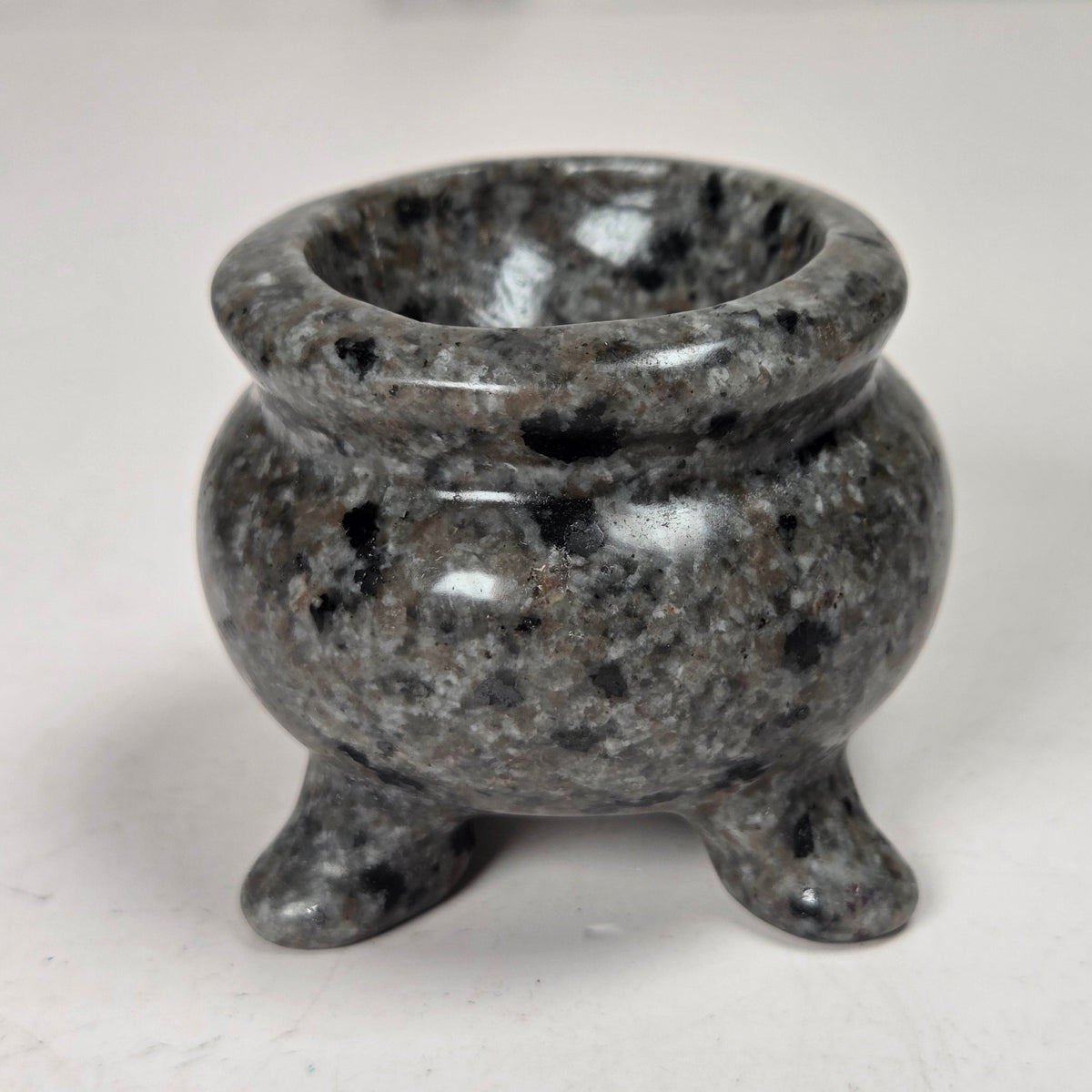 Cauldron shaped carving with grey and black spots against a white background