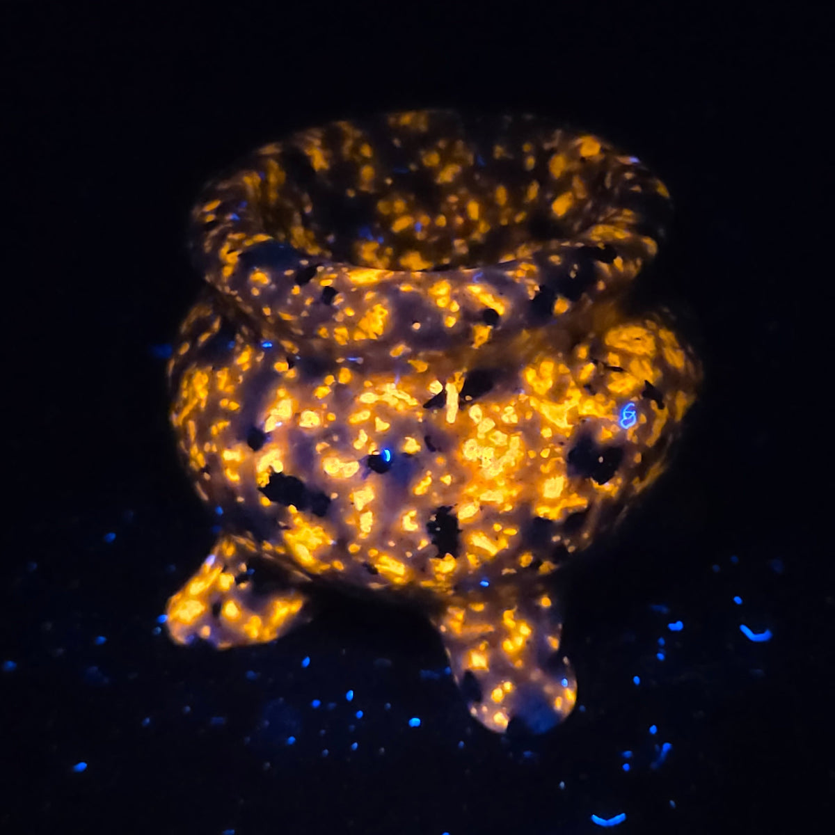 Cauldron shaped carving glowing orange under UV lighting against a black background