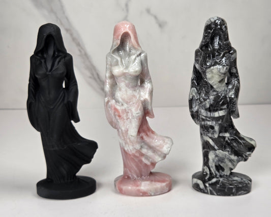 Set of 3 crystal carvings of a faceless woman wearing a flowy robe in varying colors of black, white and pink against a white background